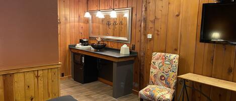 A wooden-paneled room with a kitchenette, a chair with a colorful pattern, and a television mounted on the wall.