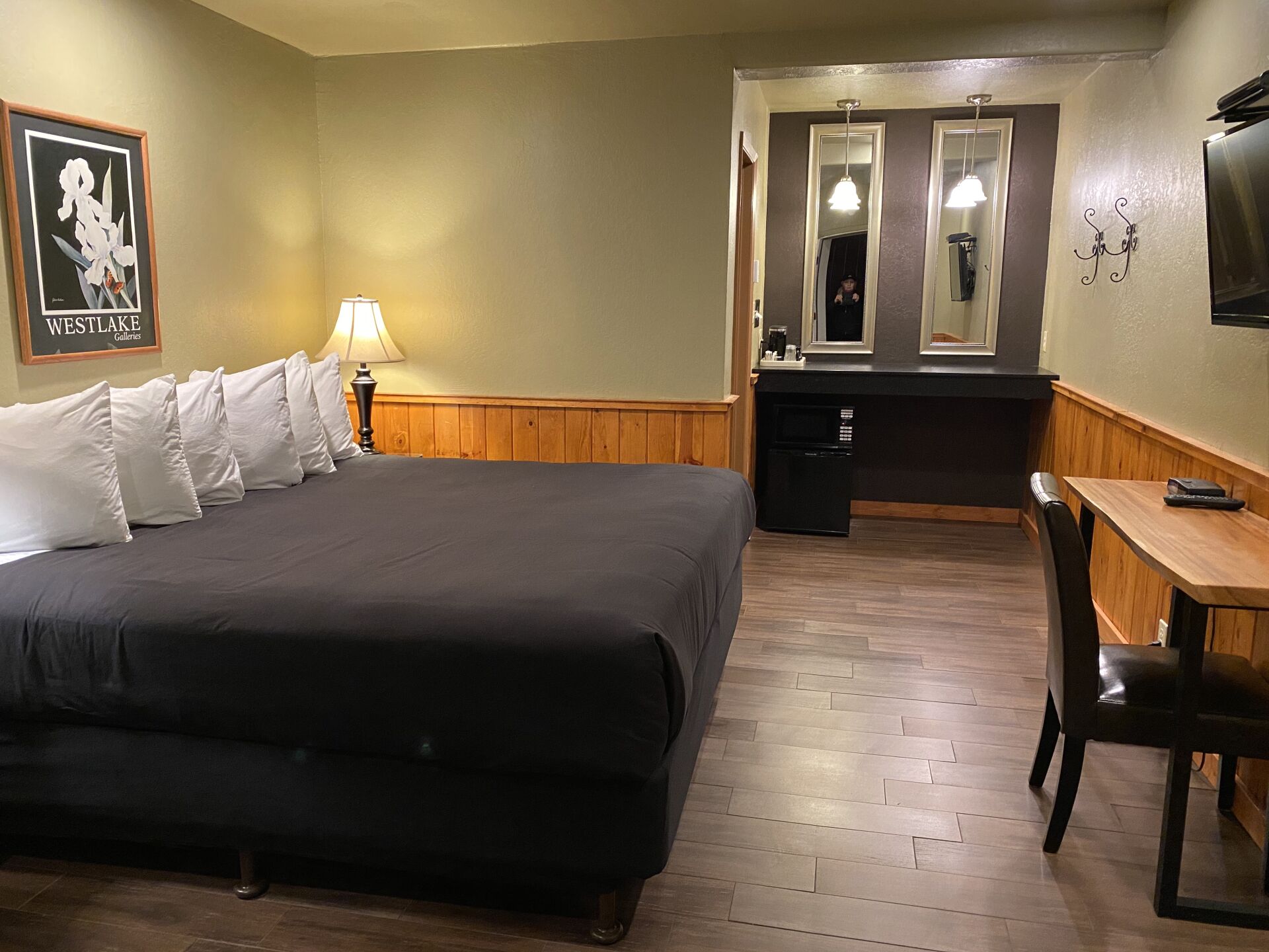 Une chambre d’hôtel avec un grand lit, un bureau, une chaise, un miroir et une petite kitchenette.