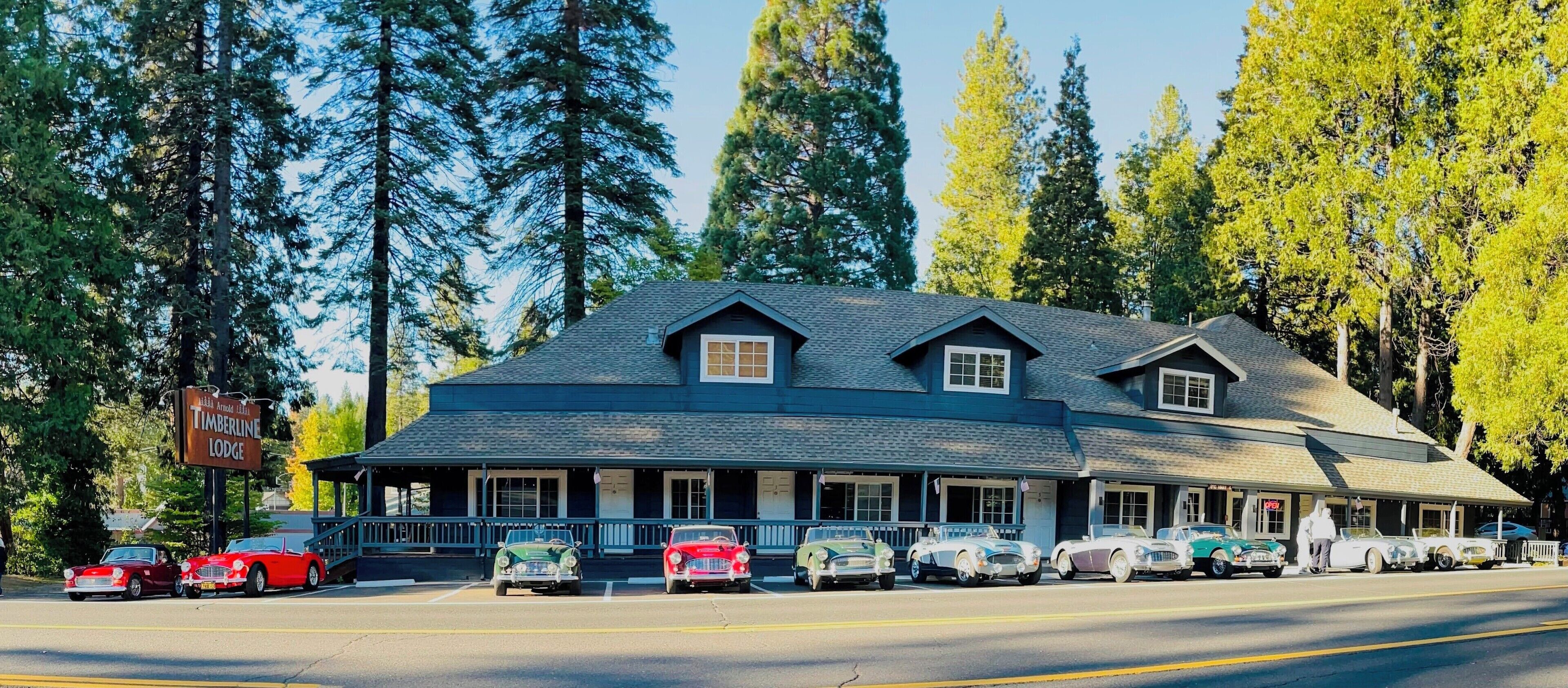 A lodge with a dark blue exterior, multiple windows, and a porch with parked vintage cars.