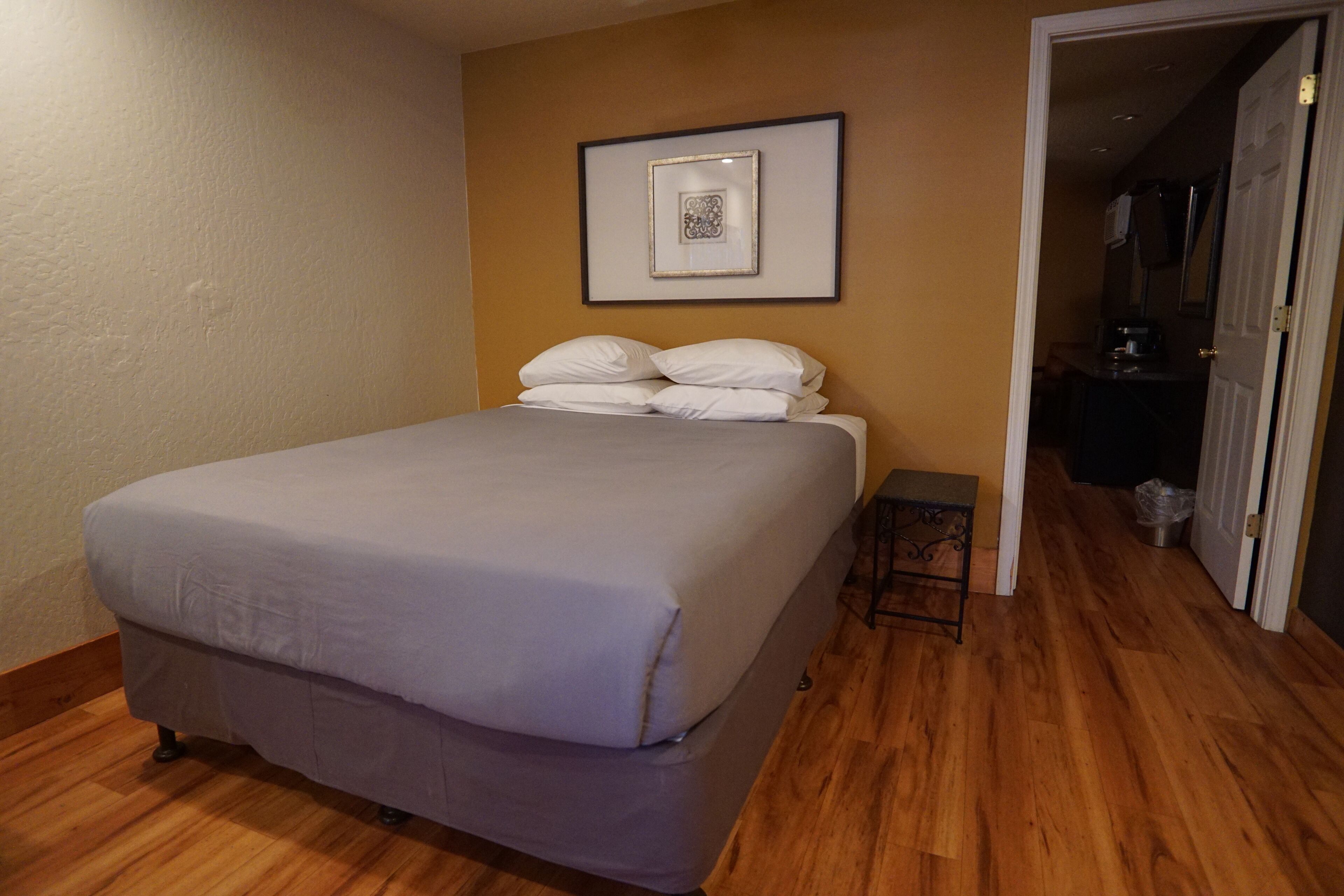 Una cama bien hecha en una habitación con suelo de madera y un cuadro en la pared.