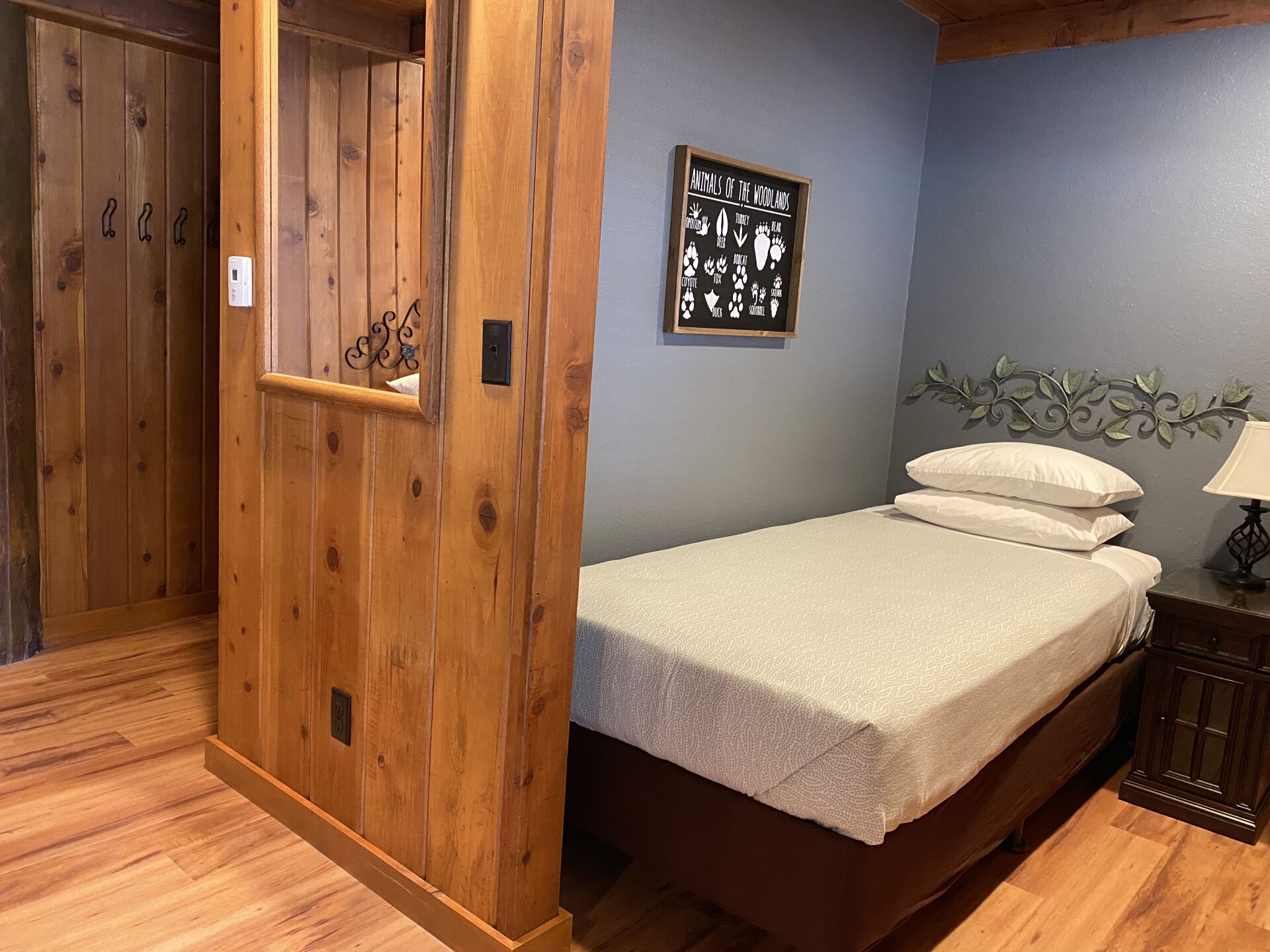 Ein Schlafzimmer mit einem Holzschrank, einem Bett mit weißer Bettwäsche, einem Wandbild mit Tiermotiven und einem Nachttisch mit einer Lampe.