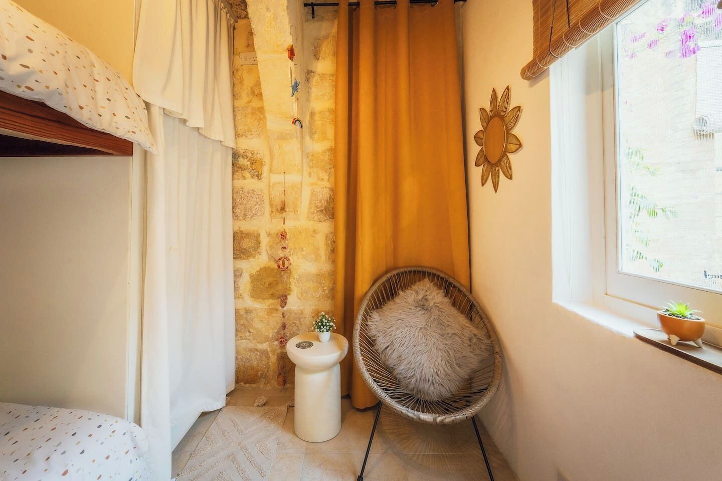Una stanza accogliente e piccola con un muro in pietra, una finestra vista e una sedia in vimini, oltre a uno sgabello bianco.