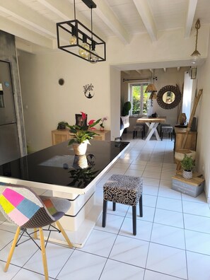 Una cocina moderna con una isla central, un comedor con mesa y sillas de madera, y vistas al exterior a través de una ventana.