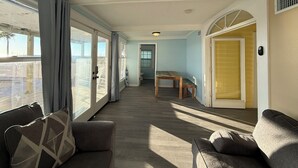 Tilava huone, jossa on suuri liukuovi, joka johtaa parvekkeelle, sekä puinen pöytä ja keltainen ovi.