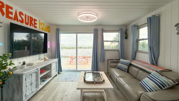 A living room with a TV, a sofa, a coffee table, and a view of the beach.