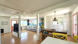 Amplia sala de estar con piso de madera, un sofá, una mesa de comedor con sillas y una zona de cocina con una parrilla.