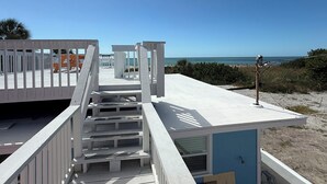 Una escalera de madera que lleva a una plataforma frente a la playa, con vista despejada al océano.