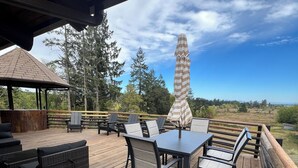Una terraza de madera con mobiliario exterior, que incluye una mesa y sillas, y una sombrilla grande.