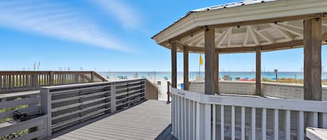 A wooden pier leading to a beach with a gazebo structure.
