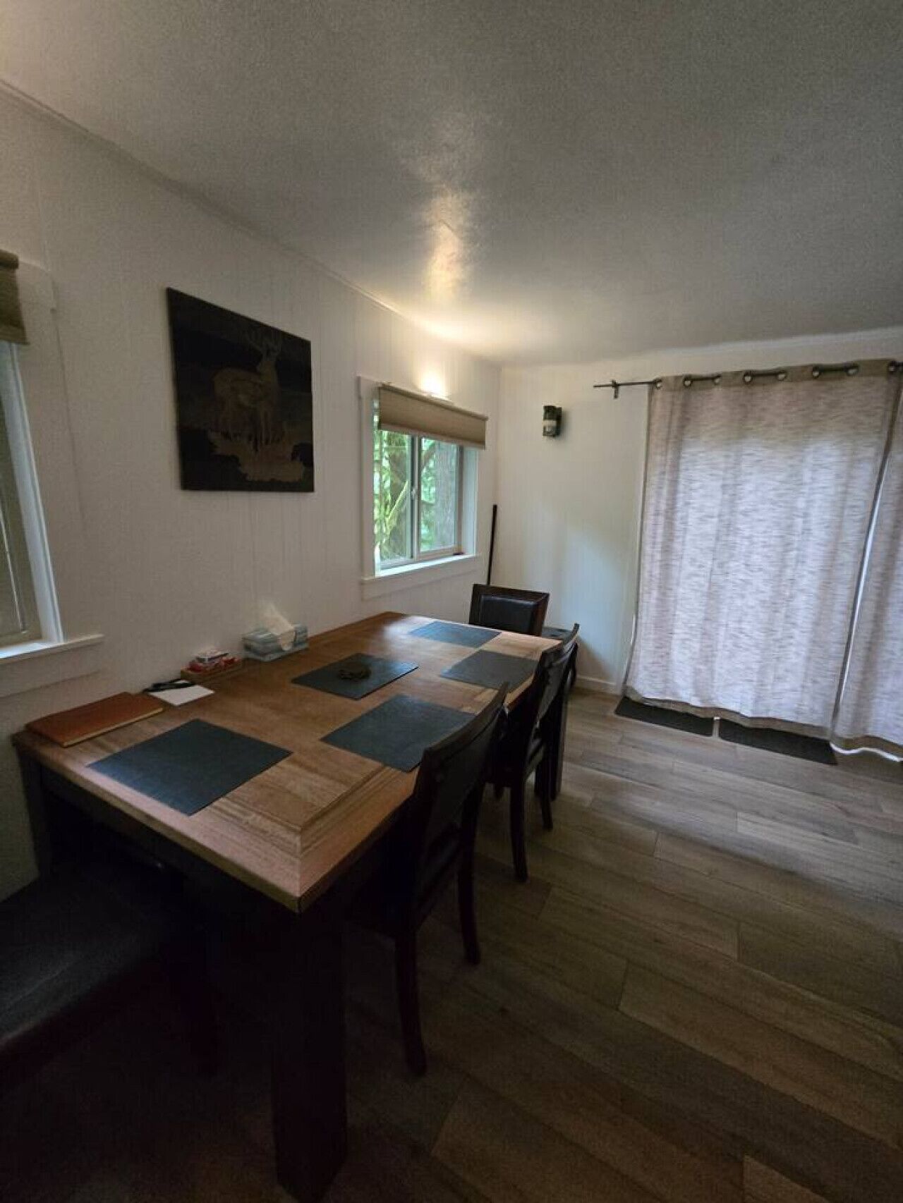 Un coin repas avec une table en bois, des chaises, une fenêtre donnant sur un beau paysage et un tableau accroché au mur.