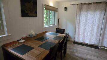 Un coin repas avec une table en bois, des chaises, une fenêtre donnant sur un beau paysage et un tableau accroché au mur.