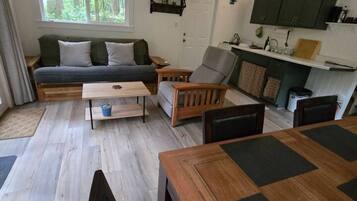 Un espace de vie compact comprenant un canapé, une table à manger, un coin cuisine et une fenêtre donnant sur un espace verdoyant.