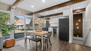 A modern kitchen with a dining area, large windows, and a view of the outdoors.