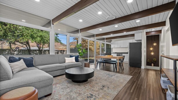 A modern living room with a gray sectional sofa, a round coffee table, and a wooden dining table.