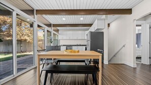 A modern kitchen with a wooden table and bench, large windows, and a view of the backyard.