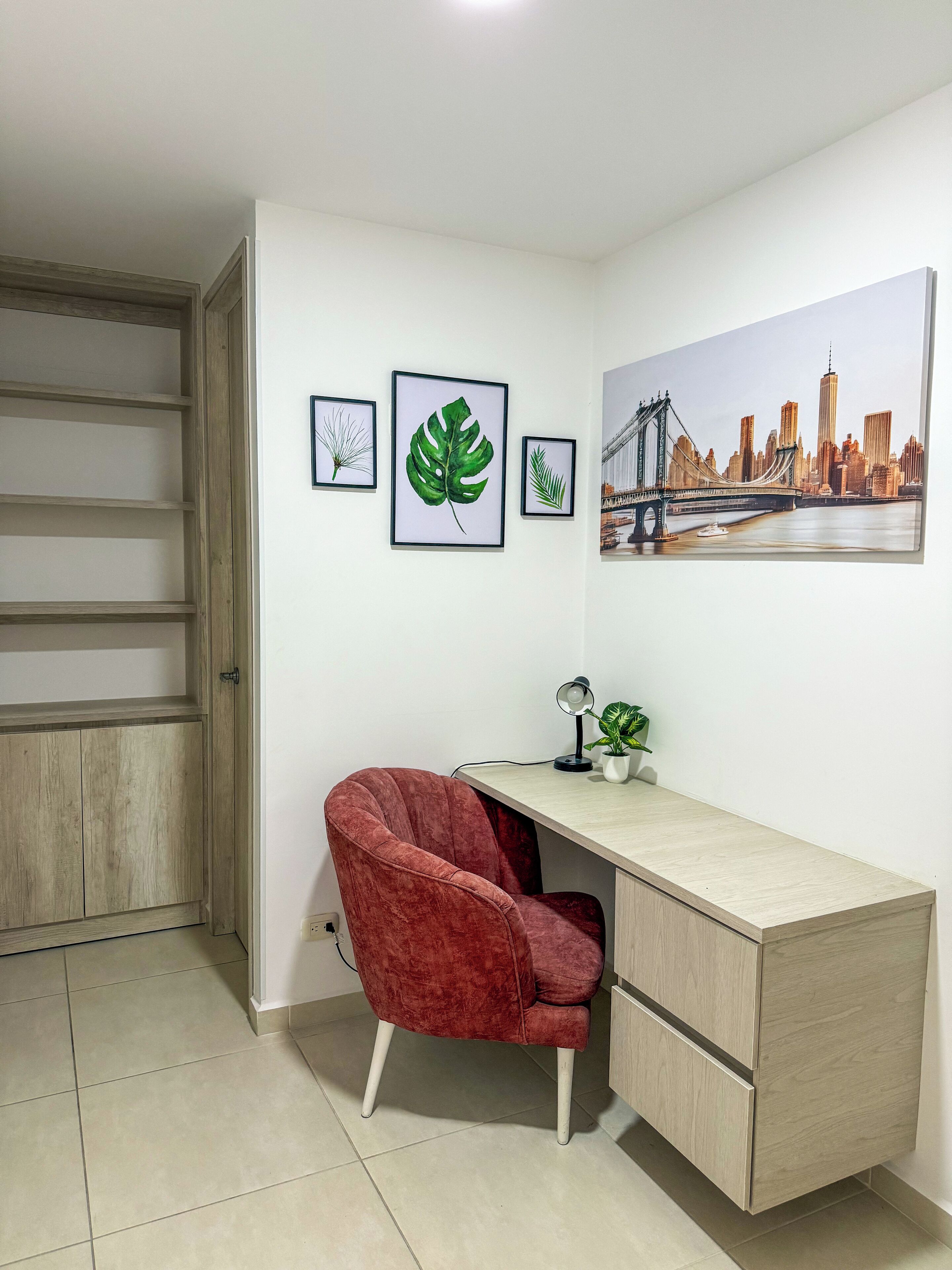Una habitación con un escritorio, una silla roja, una planta en maceta e impresiones botánicas enmarcadas en la pared.