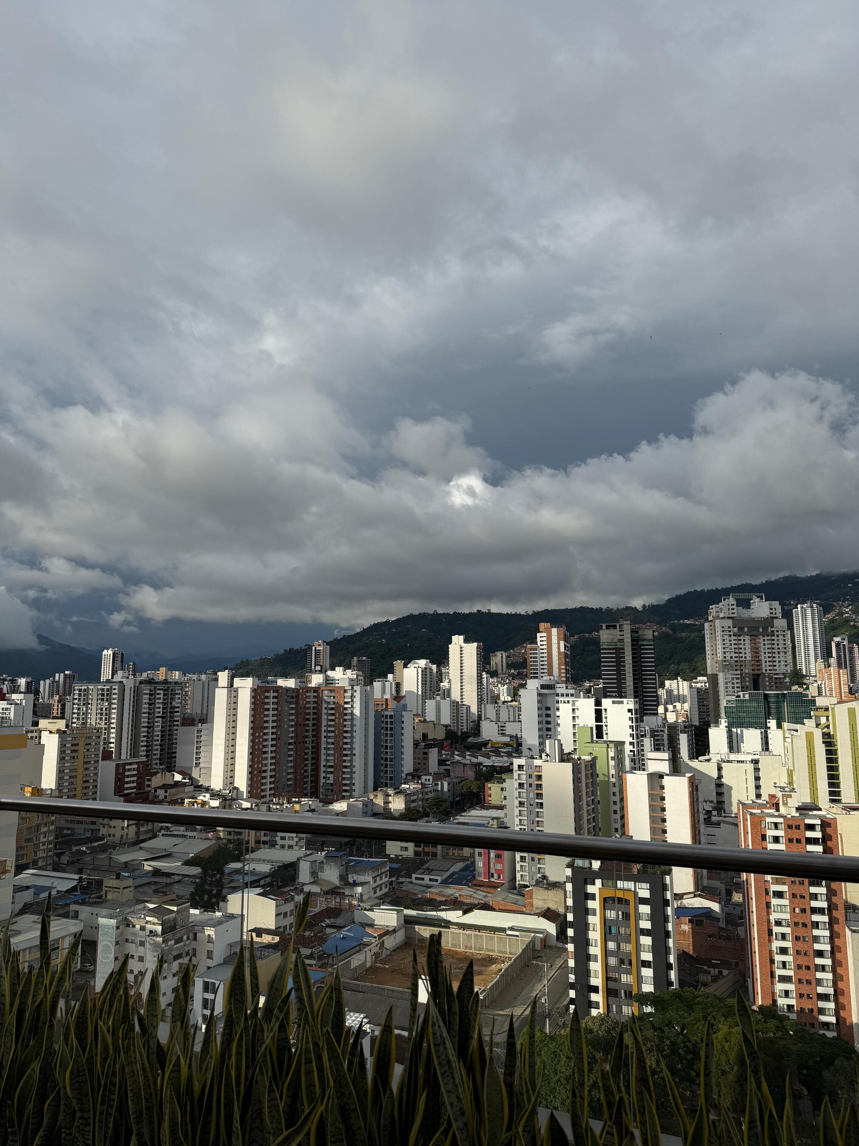 Un paisaje urbano con rascacielos, cielo despejado y una cadena montañosa distante.