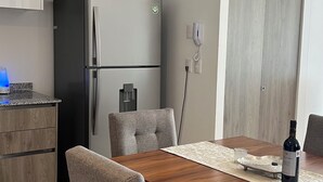 A modern kitchen with a built-in refrigerator, a wine glass on the countertop, and a dining area with a wooden table and grey upholstered chairs. - Exclusive apartment in Andares, the #1 in Guadalajara - Swimming pool - Jacuzzi - AC (Zapopan)