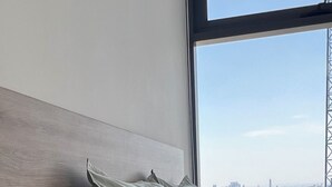 A hotel room with a bed, a desk, and a view of a cityscape through a large window. - Exclusive apartment in Andares, the #1 in Guadalajara - Swimming pool - Jacuzzi - AC (Zapopan)