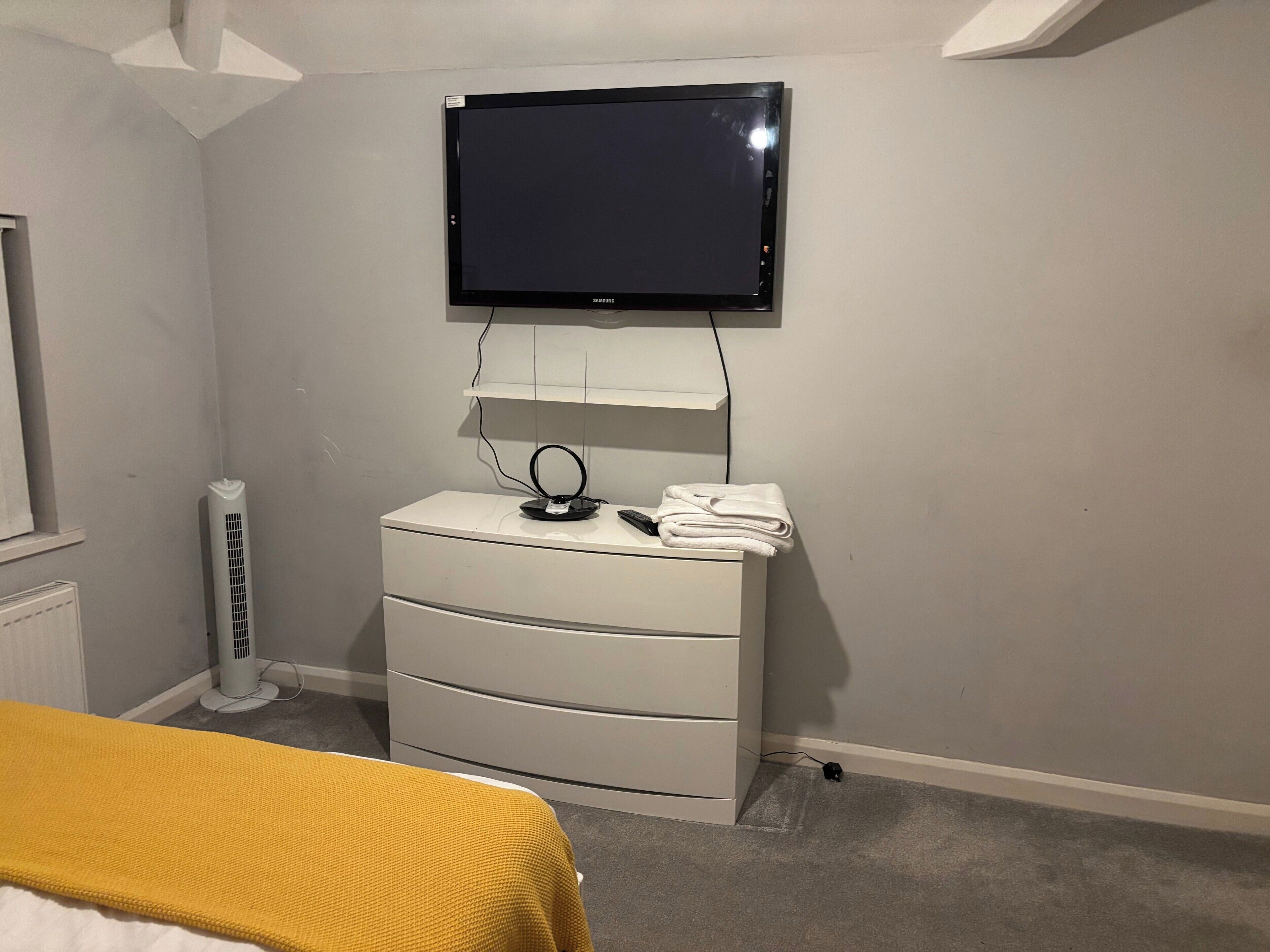A bedroom with a bed, a dresser, a TV mounted on the wall, and a radiator.