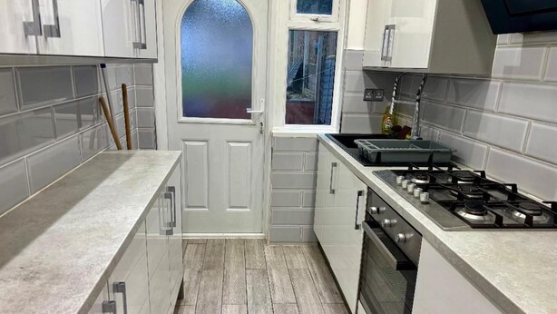 Een keuken met witte kastjes, een fornuis en een raam met gebroken glas.