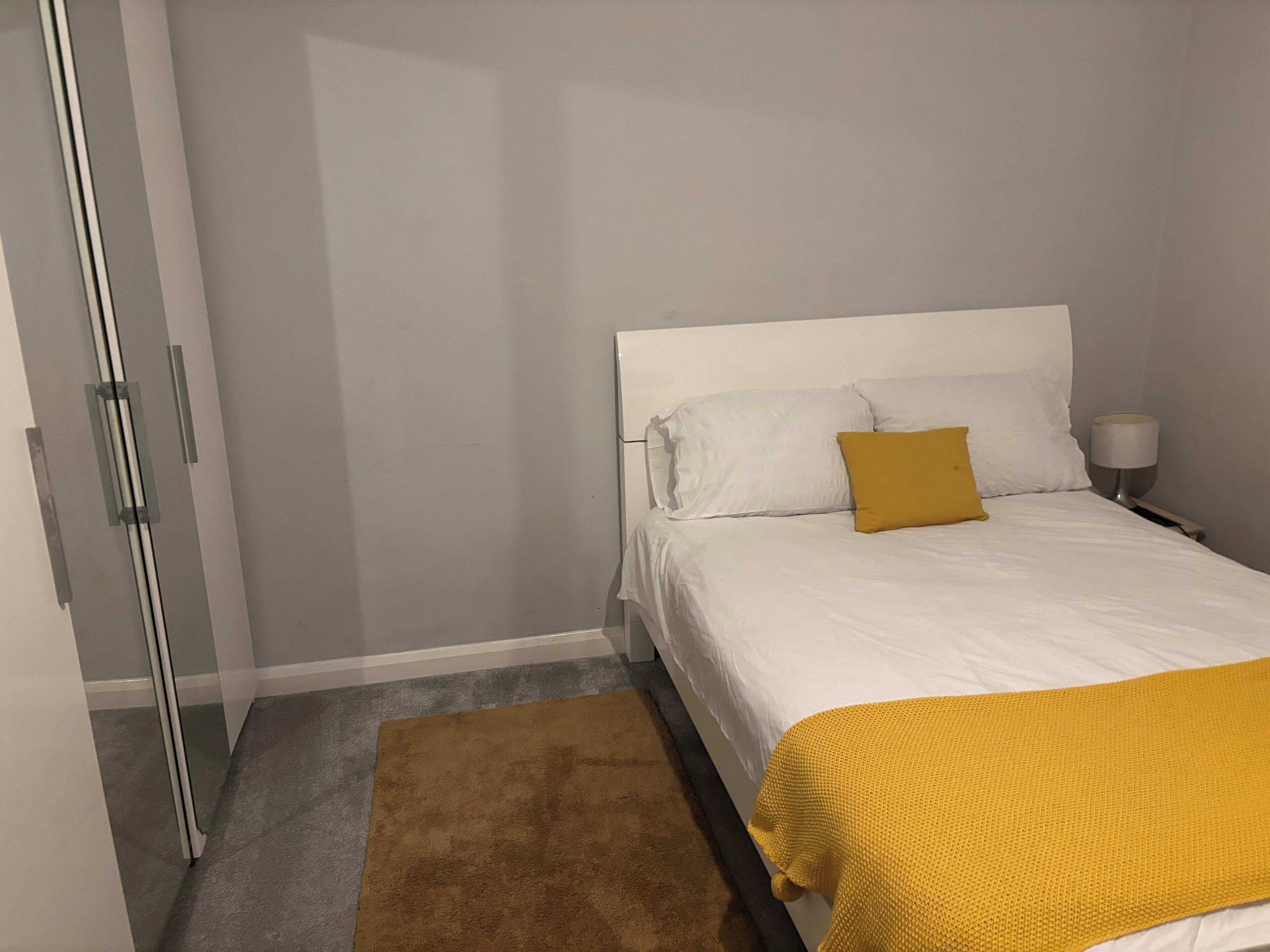 Um quarto com uma cama, mesa de cabeceira, abajur e porta.