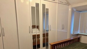 Een slaapkamer met een bed, een garderobe met spiegeldeuren en een raam met jaloezieën.