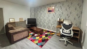 Een woonkamer met een bank, een televisie, een kleurrijk tapijt en een bureau met een stoel.