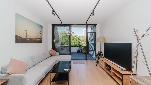 A modern living room with a sofa, coffee table, TV, and a painting of the Golden Gate Bridge. - Cosy Urban Escape near Sydneys Top Attractions (Ultimo)