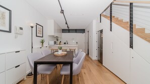 A compact kitchen with white cabinets, a wooden dining table, and a staircase with a glass railing. - Cosy Urban Escape near Sydneys Top Attractions (Ultimo)