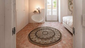 A narrow room with a patterned rug, a white chair, a bed, and a door leading to a balcony. - Danna Portuguese Design House nº 10 (Tavira)