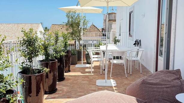 A patio with a white table and chairs, large potted plants, and a beige umbrella. - Danna Portuguese Design House nº 10 (Tavira)