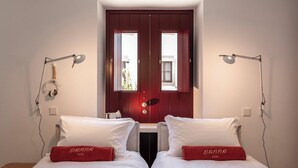 Quarto com duas camas, uma porta vermelha e duas luminárias de cabeceira.