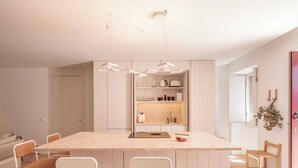 Uma cozinha moderna com uma ilha central, armários brancos e chão de tijolos.