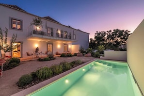 Una casa de dos pisos con piscina, mobiliario exterior y un balcón.