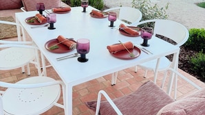 Een terras buiten met een witte eettafel, omringd door witte stoelen en comfortabele zitplaatsen.