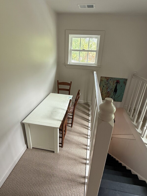 A room with a white table and chairs, a window, and a painting on the wall.