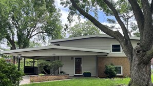 A two-story house with a covered porch, a brick foundation, and a large tree in front. - A cozy and warm 3 bedroom retreat in the heart of the Midwest (Lincoln)