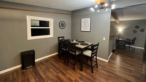 A dining area with a wooden table and chairs, a black speaker, and a window with a white frame. - A cozy and warm 3 bedroom retreat in the heart of the Midwest (Lincoln)
