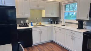 A modern kitchen with white cabinets, a black refrigerator, and a window providing a view of greenery outside. - A cozy and warm 3 bedroom retreat in the heart of the Midwest (Lincoln)