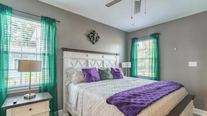 A bedroom with a bed, nightstands, a ceiling fan, and green curtains.