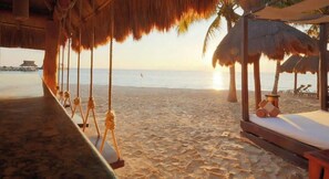 Una playa con sombrillas de paja y una estructura de madera con una cama.