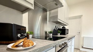 Une cuisine moderne dotée d’un four encastré, d’une hotte noire et d’un plan de travail sur lequel se trouve une assiette de croissants.