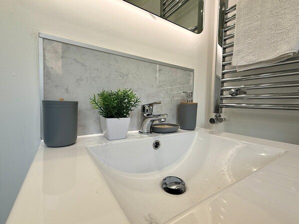 A modern bathroom with a white sink, a potted plant, and a towel rack.