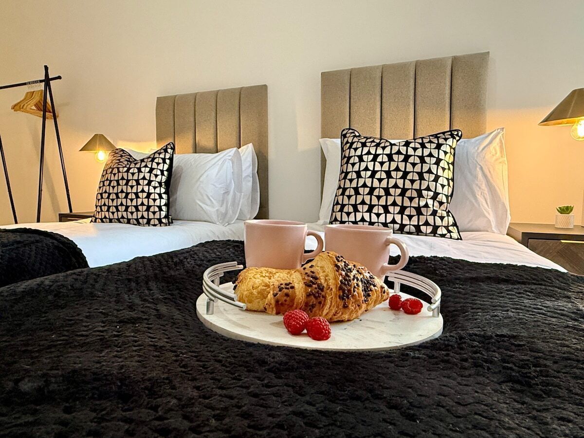Un lit avec un plateau contenant des croissants et des framboises, deux tasses et une couverture noire.