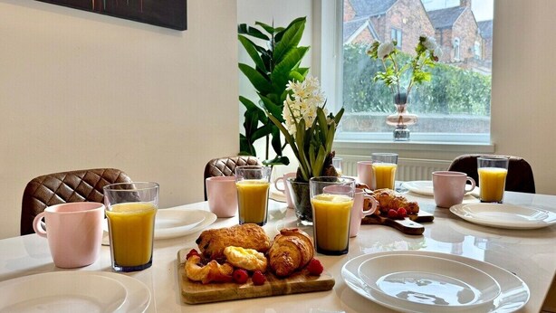 Une table de petit-déjeuner dressée avec des assiettes, des verres de jus d’orange, des croissants et un assortiment de fruits.