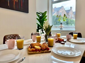 A breakfast table set with plates, glasses of orange juice, croissants, and a fruit platter.