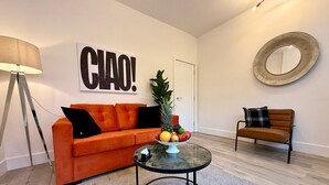 Un salon moderne avec un canapé, une table basse sur laquelle on a posé des fruits, une lampe et un miroir accroché au mur.