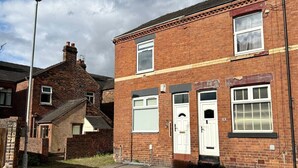 Une maison à deux étages, construite en briques, avec une porte d’entrée blanche, un petit porche et une cheminée bien visible.