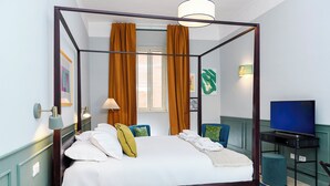 Un lit à baldaquin avec du linge de lit blanc, une table de chevet avec une lampe et un téléviseur posé sur un meuble.